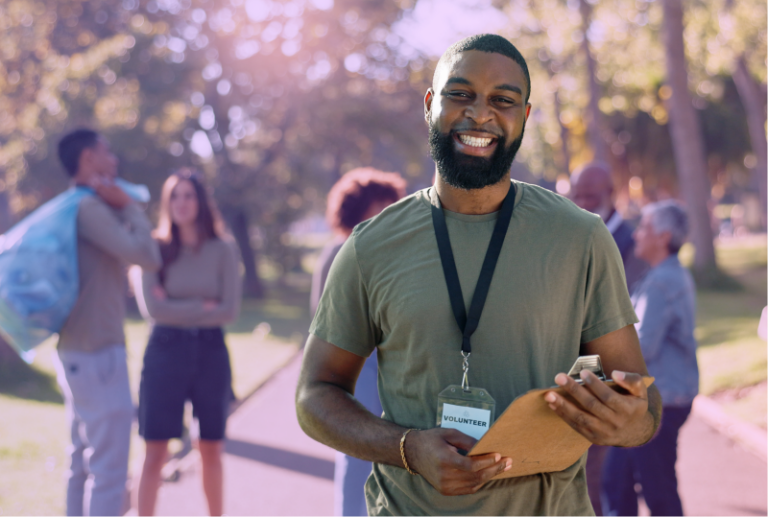 A volunteer worker is holding a clipboard in a park on a public trail and smiling