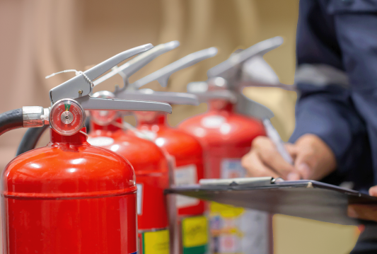 An employee is following an WHMIS training program and inspecting fire extinguishers.