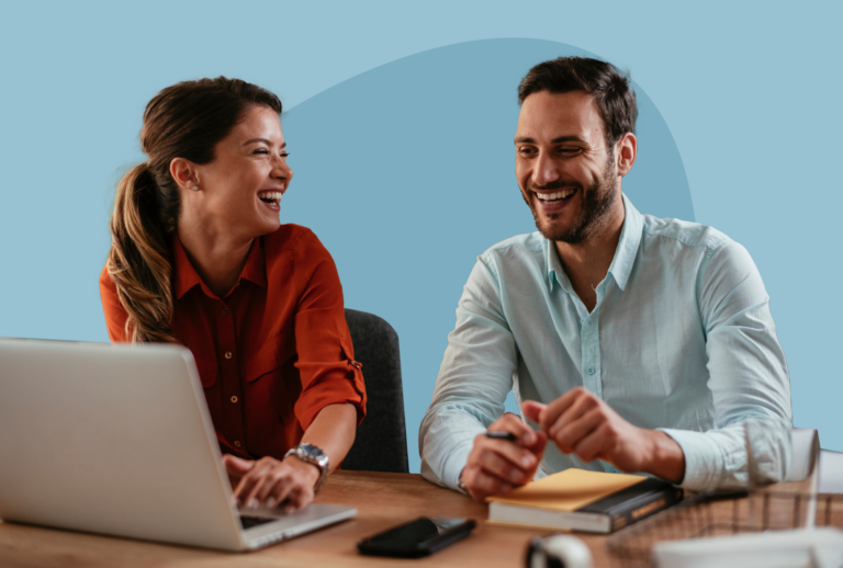 Smiling woman and man sitting next to each other at a work desk with a laptop.