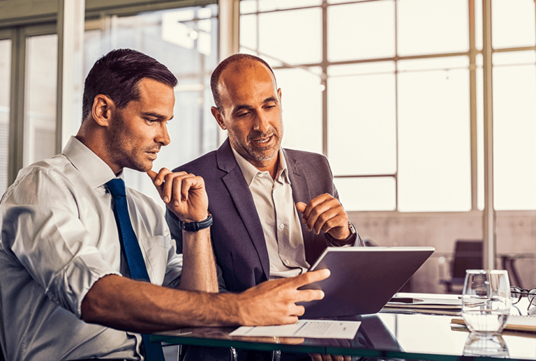 Two men sitting at a desk looking at a laptop in an office