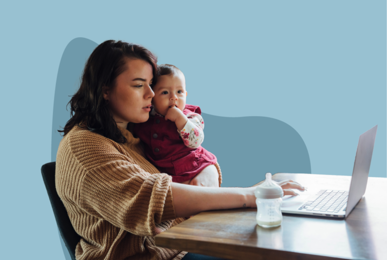 Woman working on a laptop on a desk with a baby bottle while holding a baby in her arm.