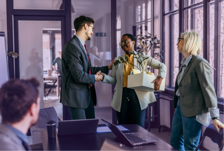 An employee has packed a box of their belongings and is leaving, while two other employees are smiling and saying goodbye.