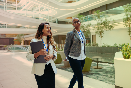 Two employees are walking side by side, smiling, while talking about how to get the most out of their Joint Health and Safety Committee.