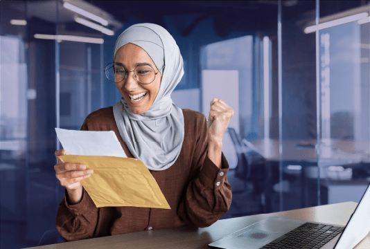 An employee is facing the camera, sitting at a desk and opening an envelope containing their pay transparency audit. They look very happy.