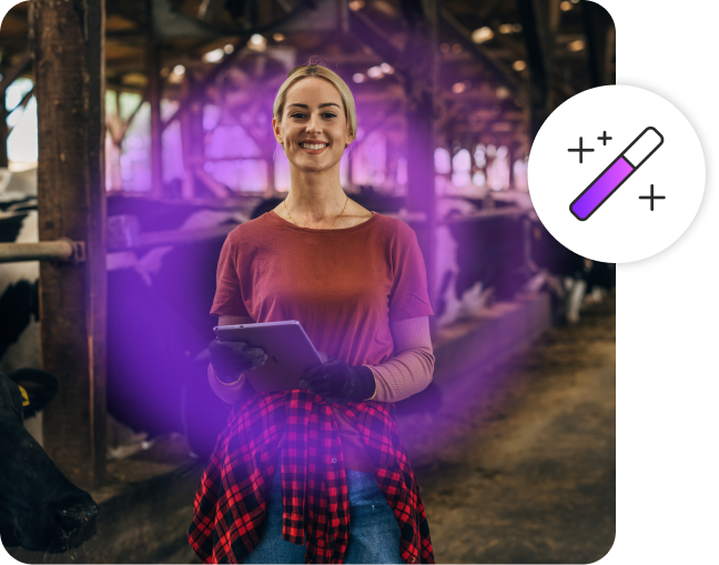 Woman smiling, wearing work clothes while holding a tablet in a cow barn.