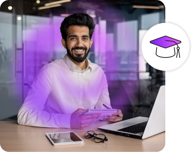 Man smiling while holding a notebook at a desk.