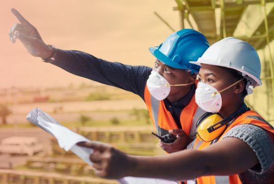 Two employees are wearing PPE, one is pointing out a hazard, the other is recording it on a clipboard.