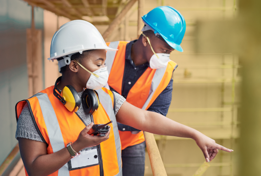 Two employees are wearing PPE and pointing out a potential hazard.