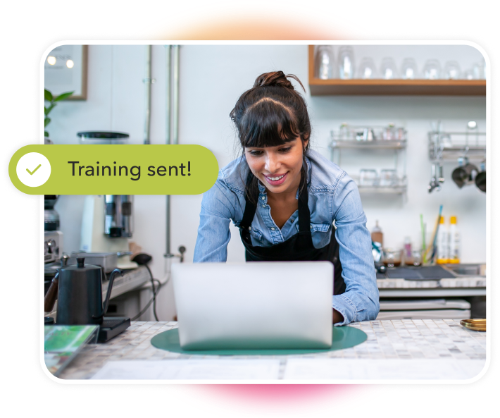 Woman in a restaurant working on a laptop, with a notification appearing above the screen that reads Training Sent!