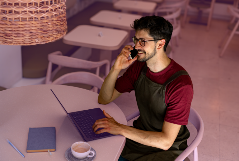 An employee is sitting at a table with a laptop while on the phone getting HR advice