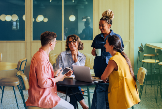 A group of employees are smiling and talking around a table in an office.