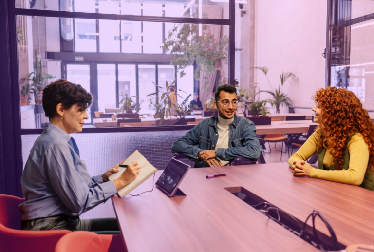 Three employees are sitting around a board room table discussing compensation and benefits