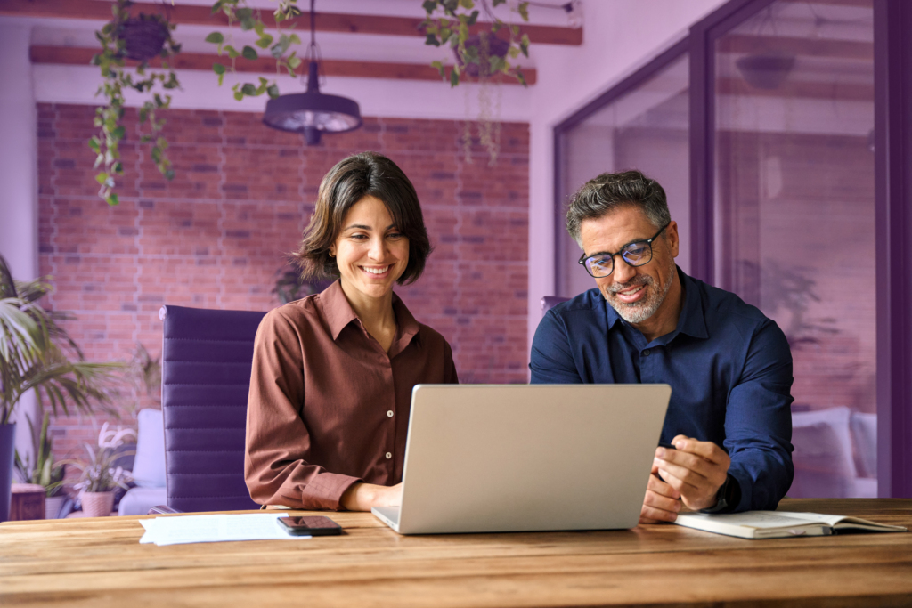 Two employees are sitting at a desk, smiling at a lap