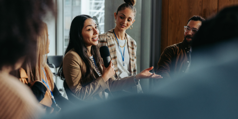 A trainer is smiling and providing in-person training to staff in a board room.