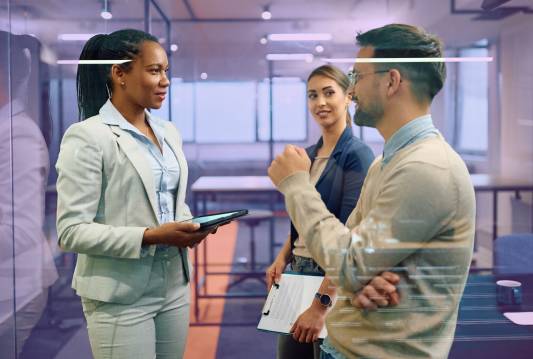 Three employees are standing, and having a respectful conversation in a meeting room