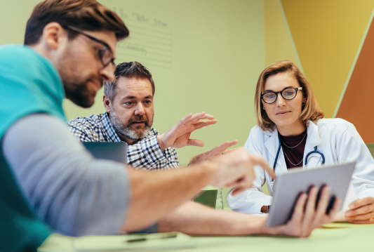 Three employees are in a board room looking at a tablet one employee is holding. They're all smiling