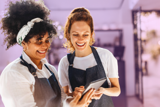 Two employees are smiling and standing next to each other.