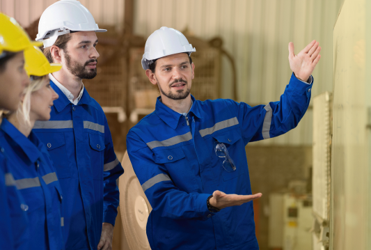 One employee in high-vis safety clothing is training three other employees. They are all looking at a whiteboard.