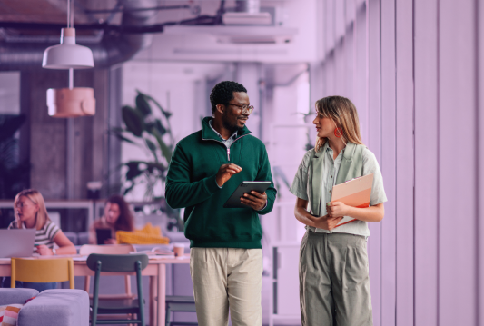 Two employees are walking beside each other in the workplace while discussing knowledge transfer plans.
